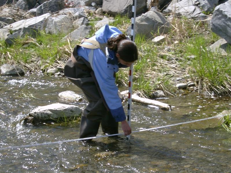 Student in waders in stream with meter stick