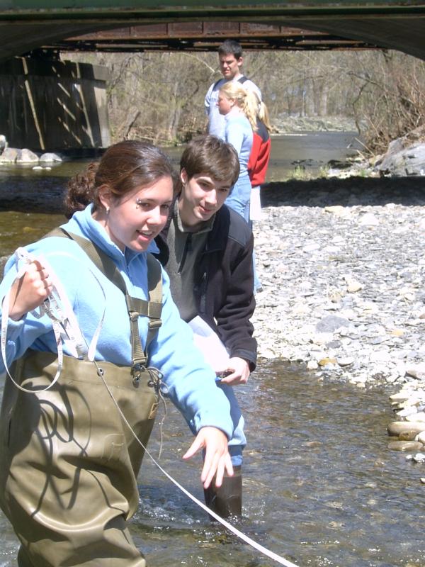 Two students in stream with tape measure